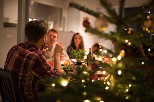 Gjeng med venner rundt et bord og koser seg. Juletre i forgrunnen