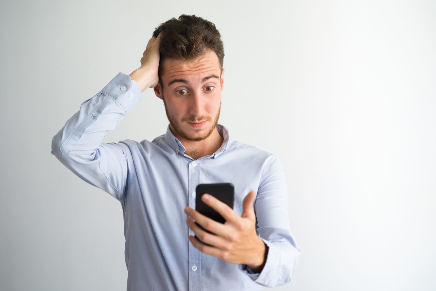 Mann klør seg i hodet og ser på mobilen